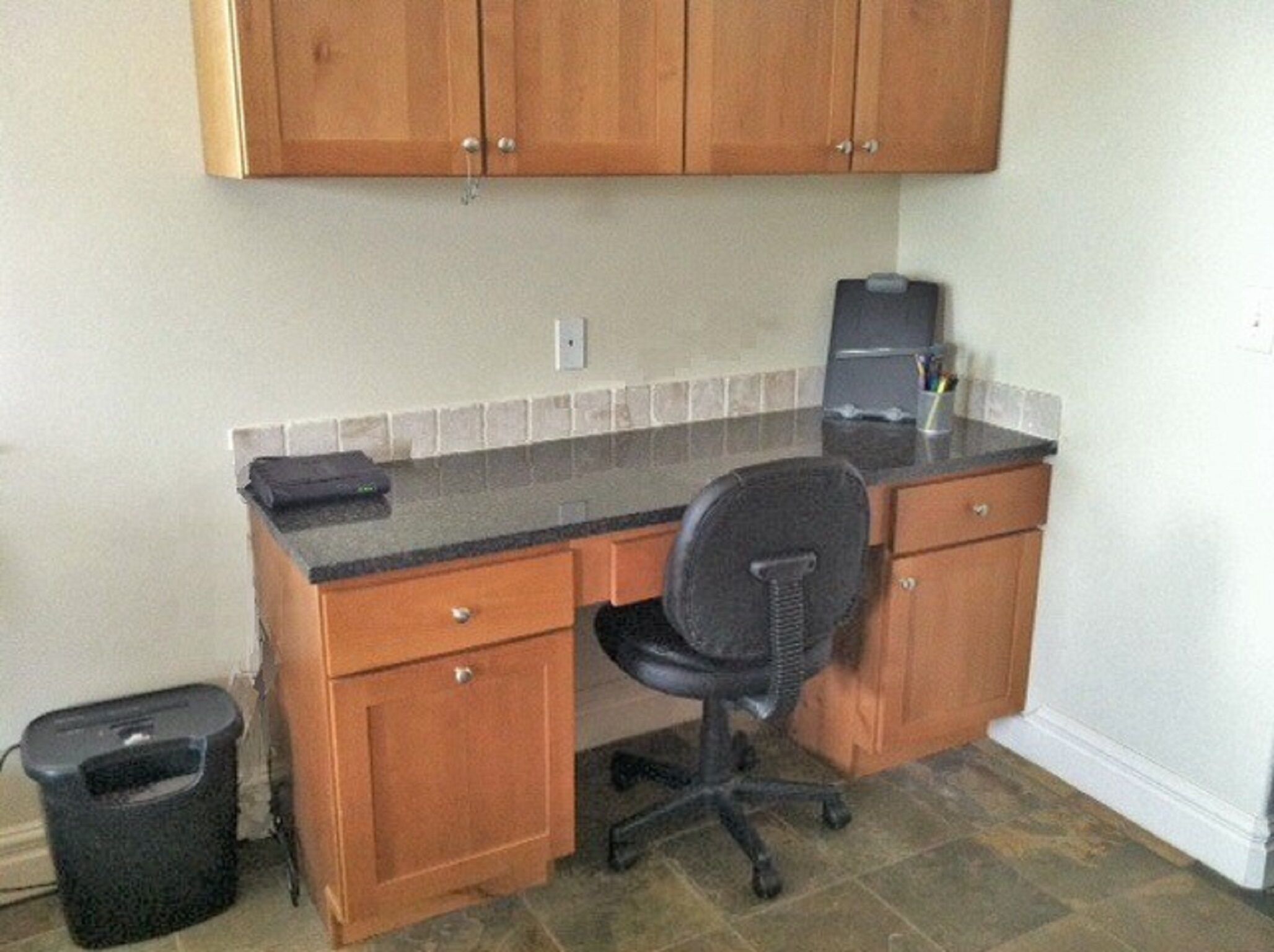 A small kitchen with wooden cabinets, a black office chair, and a coffee maker on the counter.