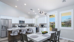 A modern kitchen with white cabinets, stainless steel appliances, and a dining area with a marble countertop and grey chairs. - Modern Wine Country Escape in the Verde Valley + Fire Pit + Sleeps 6+ (Cottonwood)
