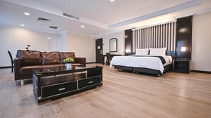A modern hotel room with a large bed, a sofa, a coffee table, and a desk with a chair.