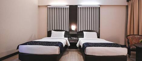 A hotel room with two beds, a nightstand, and a chair.