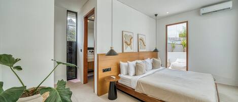 A modern bedroom with a large bed, a bedside table, a potted plant, and a view of the outdoors.