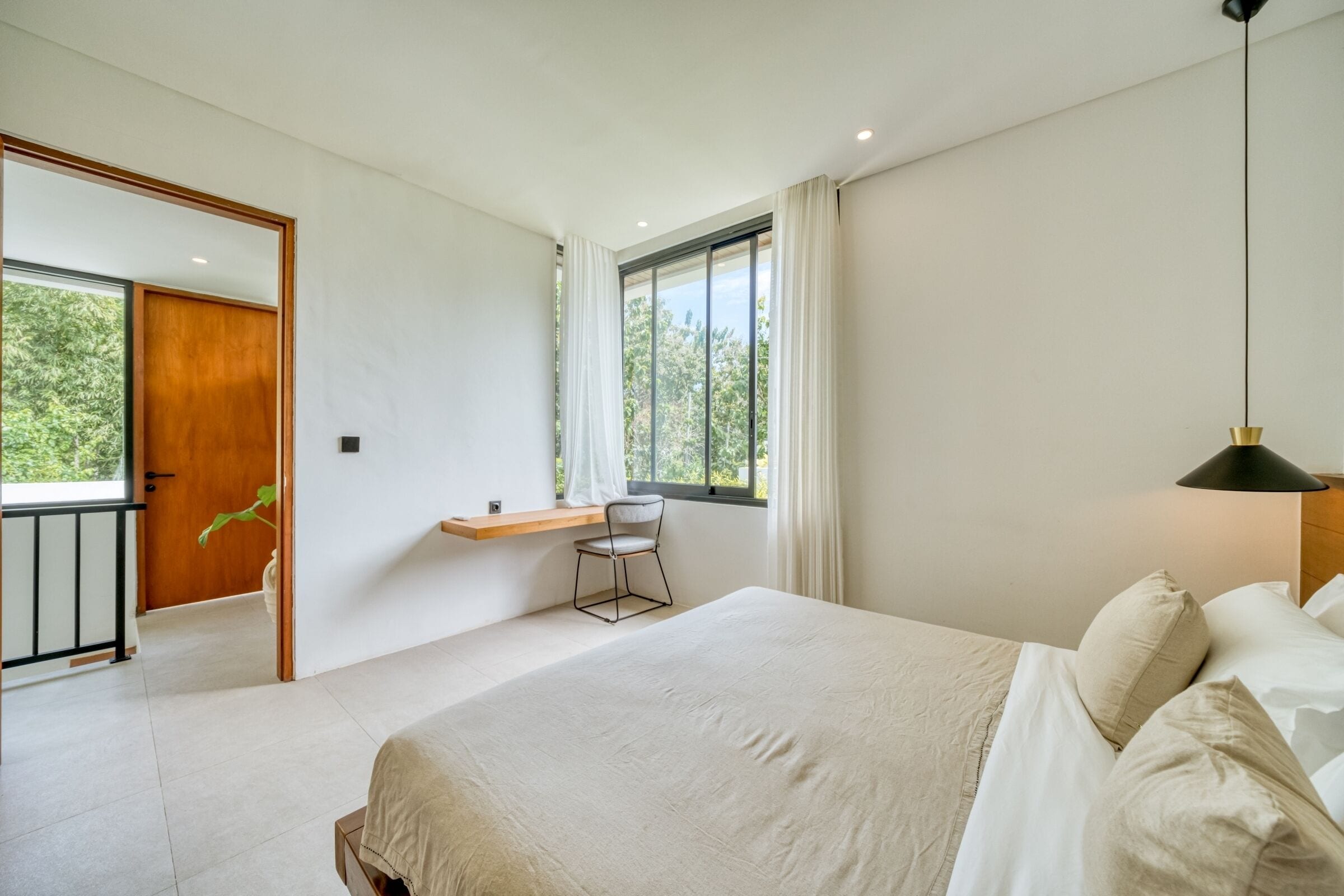 A bedroom with a large bed, a desk, and a window with curtains.