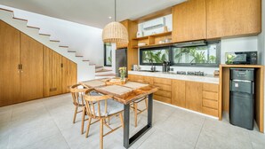 Une cuisine moderne avec des meubles en bois, un coin repas comprenant une table et des chaises, une cuisinière encastrée et un réfrigérateur.