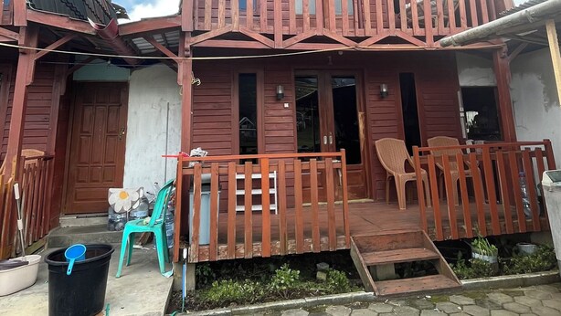 A two-story wooden house with a balcony, a front door, and a small porch area. - Quen'z Cabin (Kejajar)