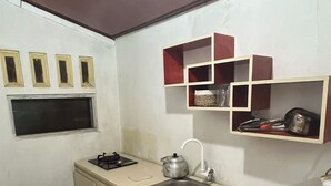 A compact kitchen with a sink, stove, and a small window. There are wooden shelves above the sink and a trash bin to the right. - Quen'z Cabin (Kejajar)