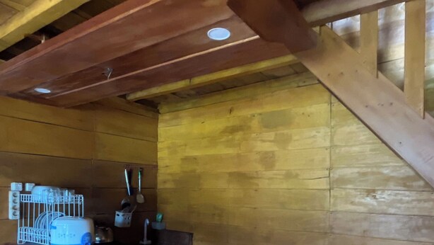 Een houten interieur met een bar in het midden, houten balken aan het plafond en een betegelde vloer.