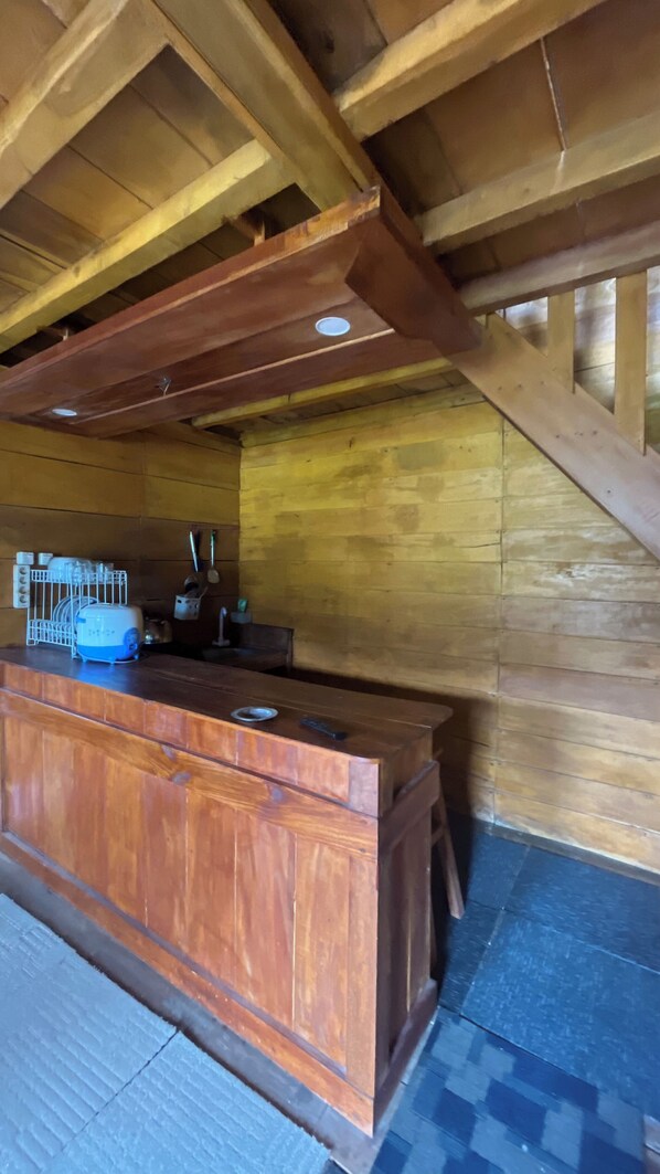 Un intérieur en bois avec un bar central, des poutres en bois au plafond et un sol carrelé.