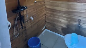 Een kleine badkamer met houten lambrisering, een douche, een blauwe emmer en een toilet.