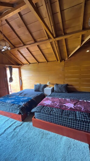 Une chambre dans un chalet en bois, avec deux lits, une table de chevet et un luminaire suspendu.