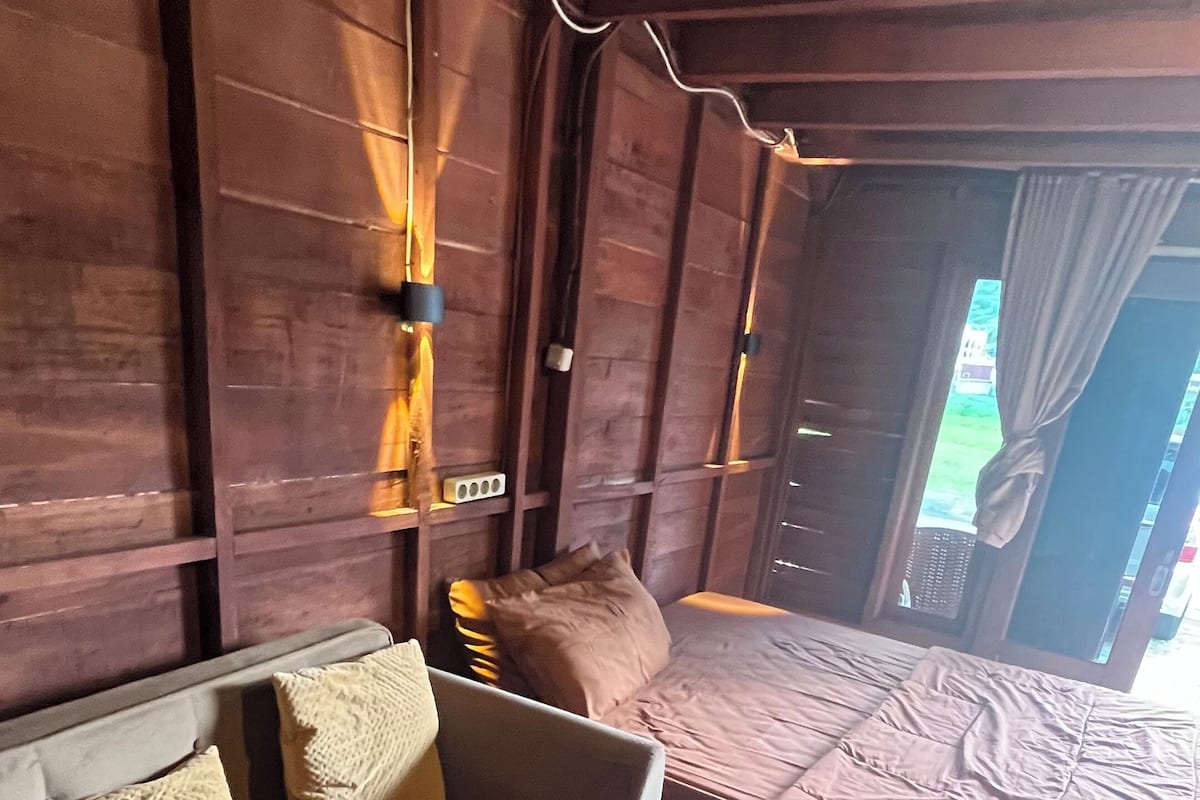 A room with a sofa, a bed, a patterned rug, and wooden walls.