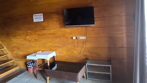 Een knus ingerichte kamer met een houten plafond, een bed met een kleurrijke quilt, een aan de muur bevestigde televisie en een klein tafeltje met een stoel.