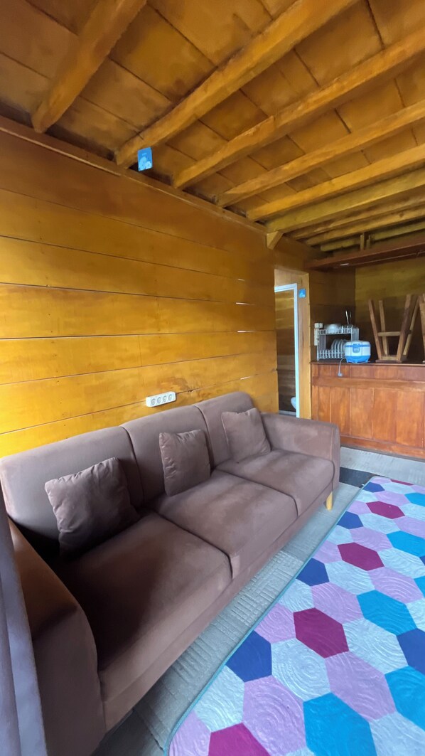 Ein Zimmer mit braunem Ledersofa, einem gesteppten Teppich, Holzwänden und einer Bar mit Geschirr.