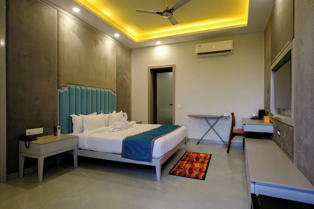 A modern hotel room with a bed, bedside table, desk, chair, and a ceiling fan.