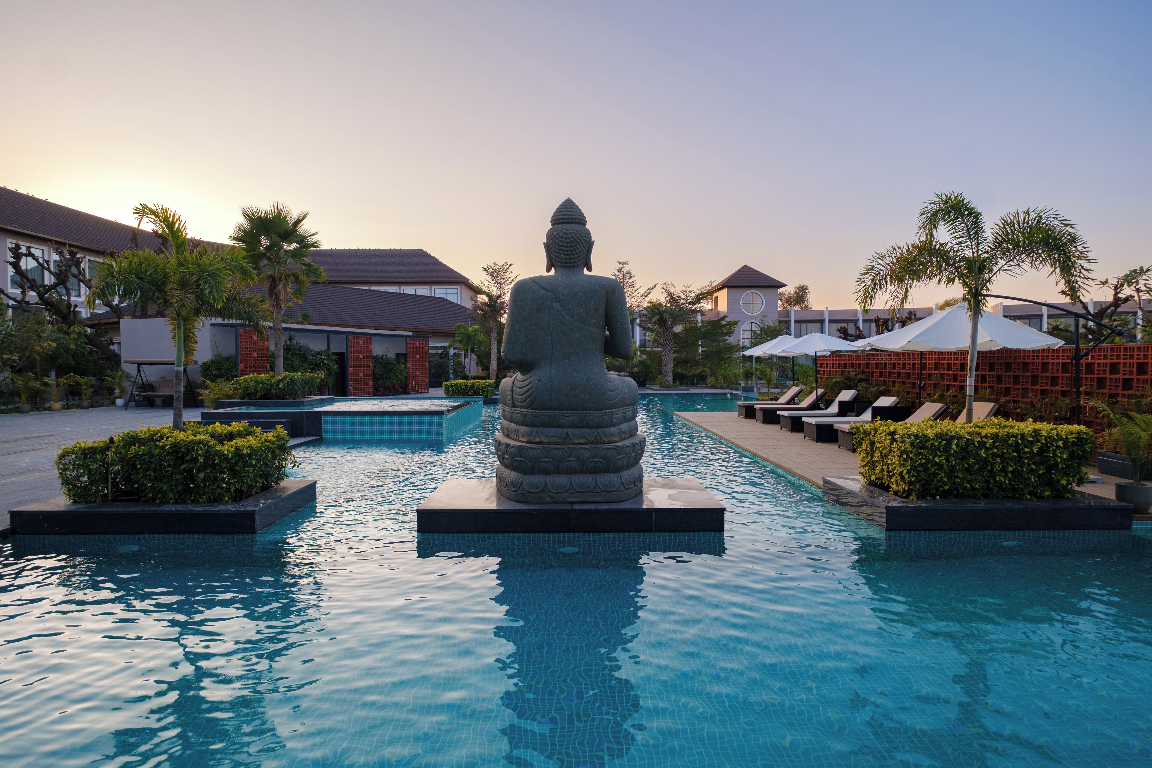 A Buddha statue in a pool with lounge chairs and palm trees.