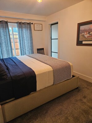 Ein Schlafzimmer mit einem Bett, einem Sessel, einem gerahmten Bild an der Wand und einem Fenster mit Vorhängen.