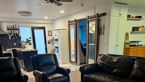 A living room with a dark brown coffee table, black leather sofas, and a black leather armchair. There is a kitchen area in the background with a stove and cabinets. - Family- and Pet-Friendly Downtown Home, Close to Everything (Stevensville)