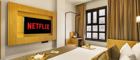 Habitación de hotel con una cama grande, un televisor montado en la pared, una mesita de noche y una ventana con cortinas.