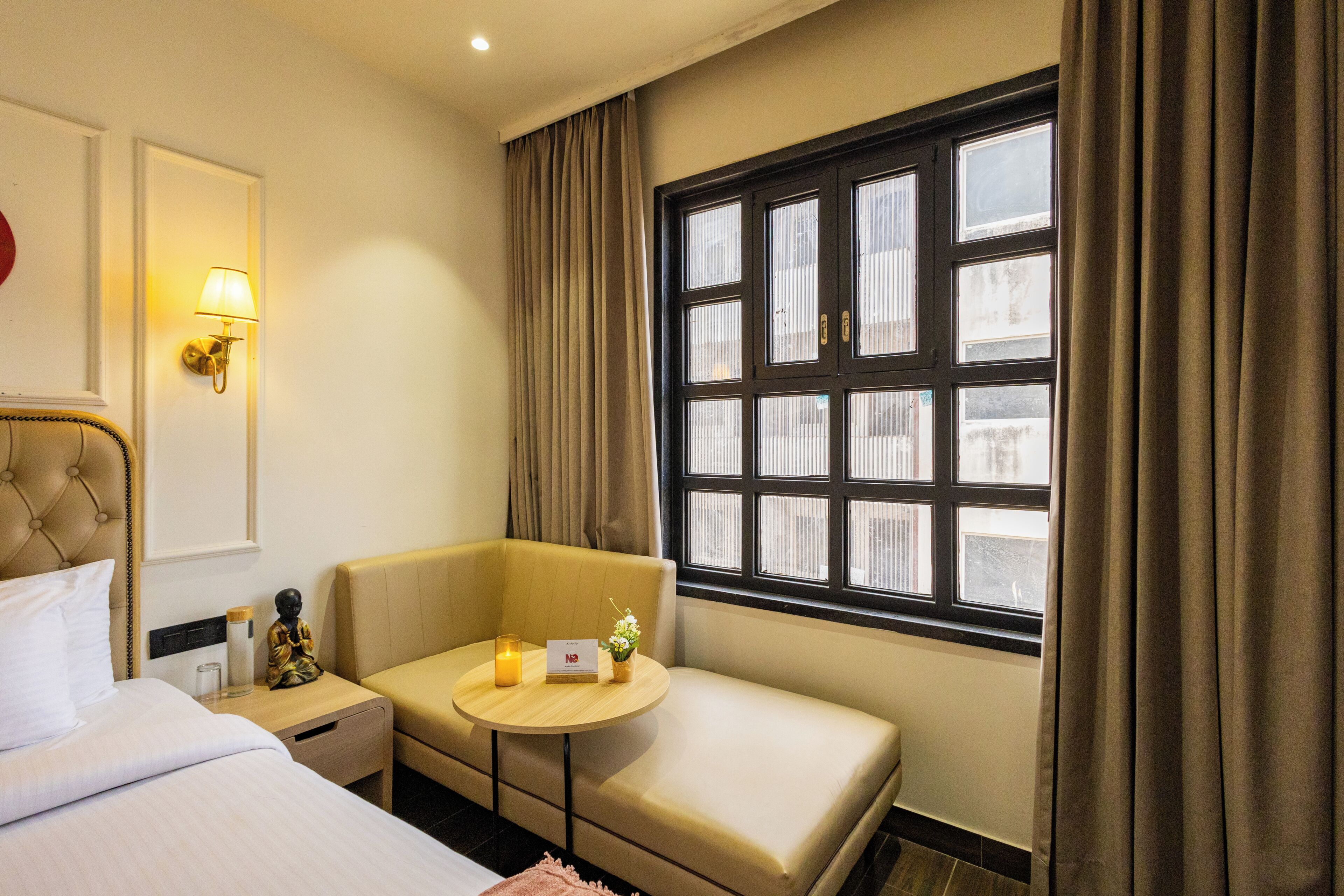 Une chambre d’hôtel avec un lit, un canapé, une petite table avec une lampe, une lampe fixée au mur et une fenêtre avec des rideaux.