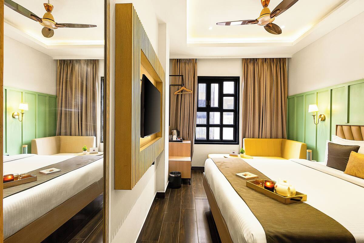 A hotel room with two beds, a TV, a ceiling fan, a window, and a tray with candles.