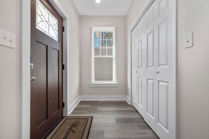 A hallway with a brown door, a window with blinds, and a white door with a doormat. -  Diamondhead Retreat – Perfect for Spring Break near Lake Catherine State Park ! (Hot Springs National Park)