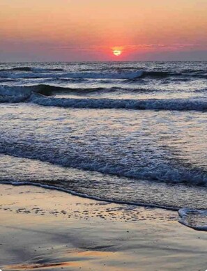 Ein Strand mit Wellen und einem Sonnenuntergang.