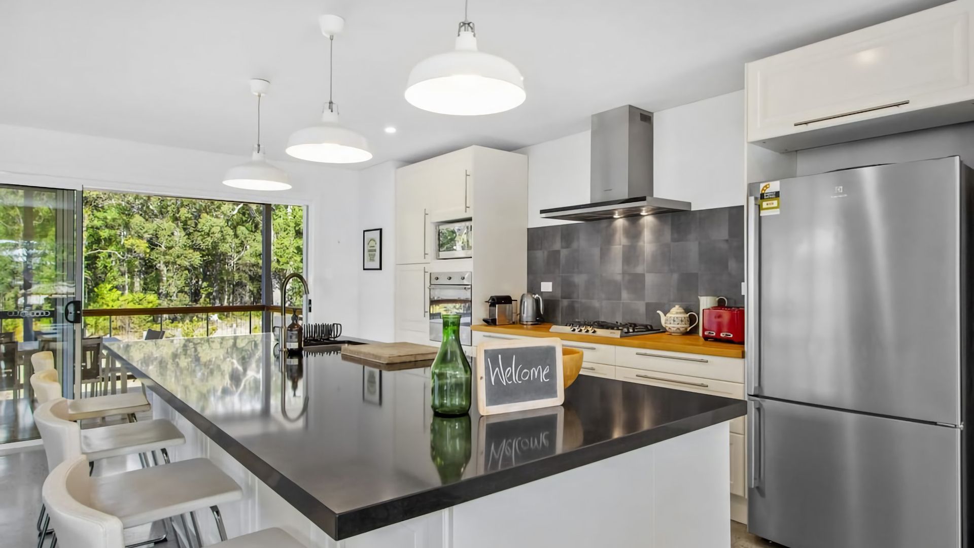 A modern kitchen with a central island, stainless steel appliances, and a view of greenery outside.
