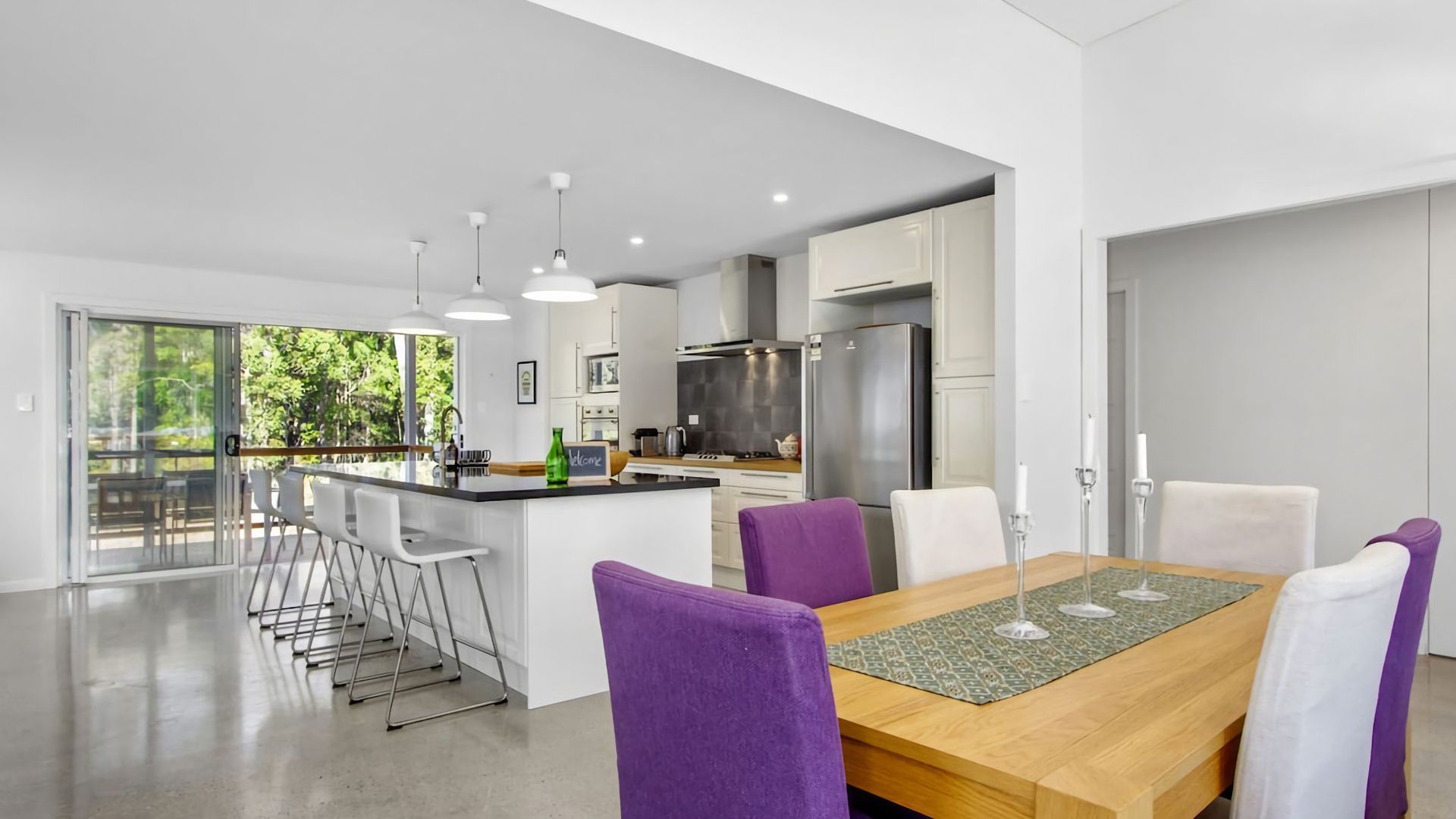 A modern kitchen with a central island, bar stools, and a dining table with purple chairs.