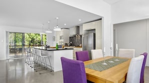 Una cocina moderna con una isla central, taburetes de bar y una mesa de comedor con sillas moradas.