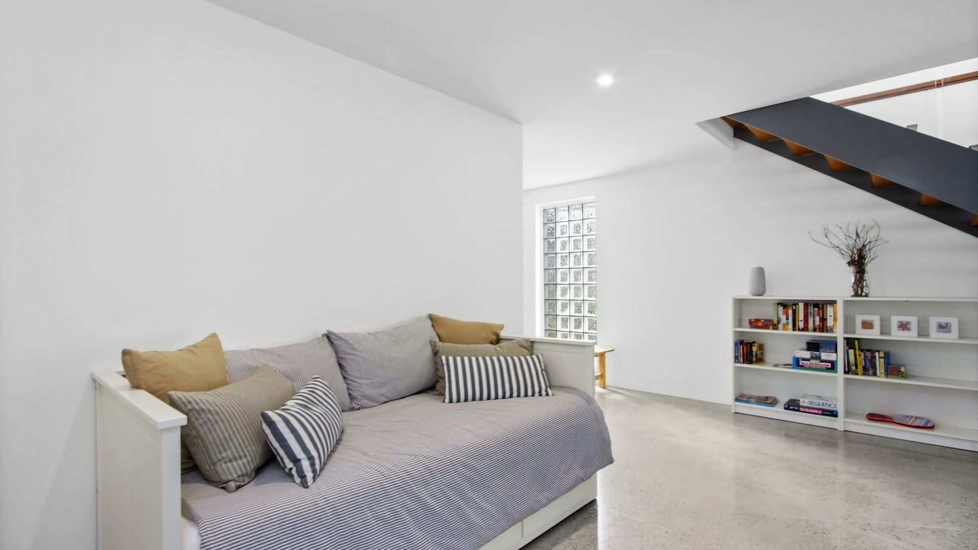 A modern living room with a sofa, cushions, a bookshelf, and a staircase.