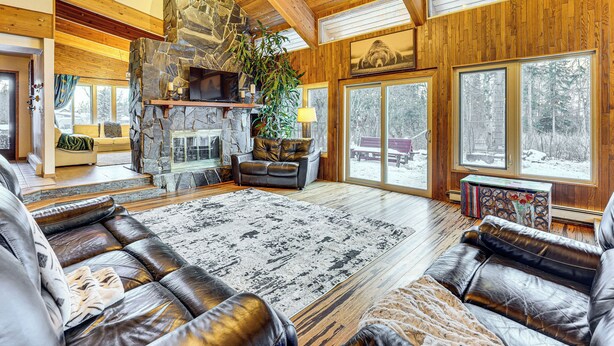 Ein großzügiges Wohnzimmer mit Kamin aus Stein, Ledersofas und großen Fenstern mit Blick ins Freie.