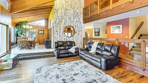 Ein großzügiger Wohnbereich mit hohen Decken, Holzbalken und einem Kamin. Es gibt einen Essbereich mit Tisch und Stühlen, sowie ein großes Fenster, das für natürliches Licht sorgt.