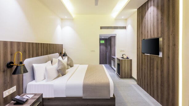 A modern hotel room with a large bed, a desk with a lamp, a flat-screen TV mounted on the wall, and a ceiling fan. - Enrise By Sayaji Bareilly (Bareilly)