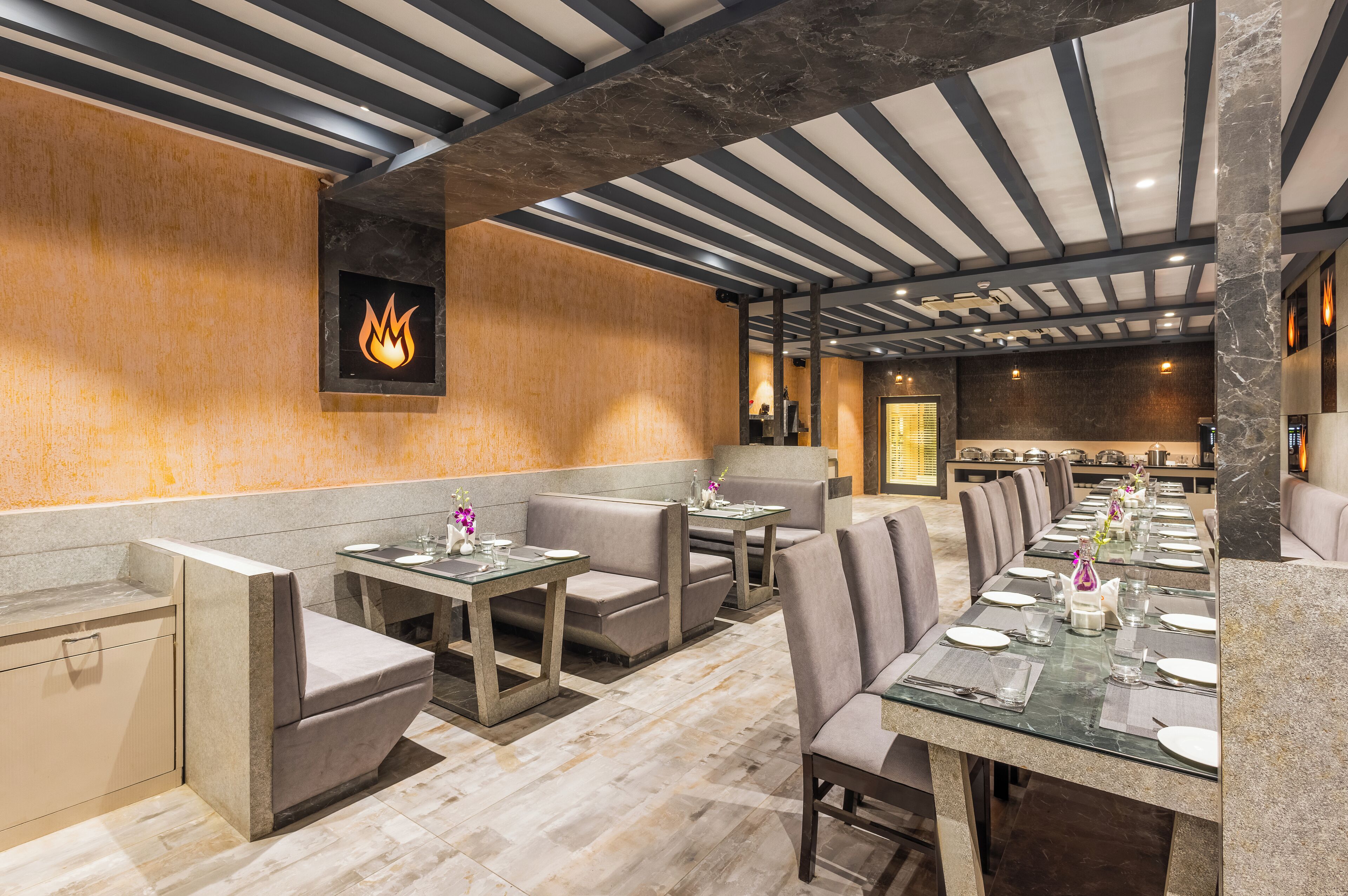 A restaurant with a long communal table, booths, and a modern ceiling design.
