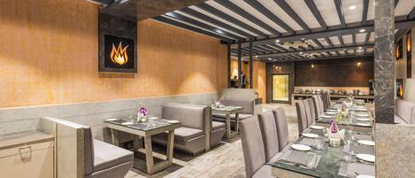 A restaurant with a long communal table, booths, and a modern ceiling design.