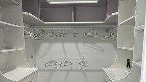 Un placard moderne et bien aménagé, avec des étagères, des tiroirs et un espace pour suspendre les vêtements, le tout dans des tons blancs, agrémenté d’un puits de lumière et d’un revêtement de sol en marbre.