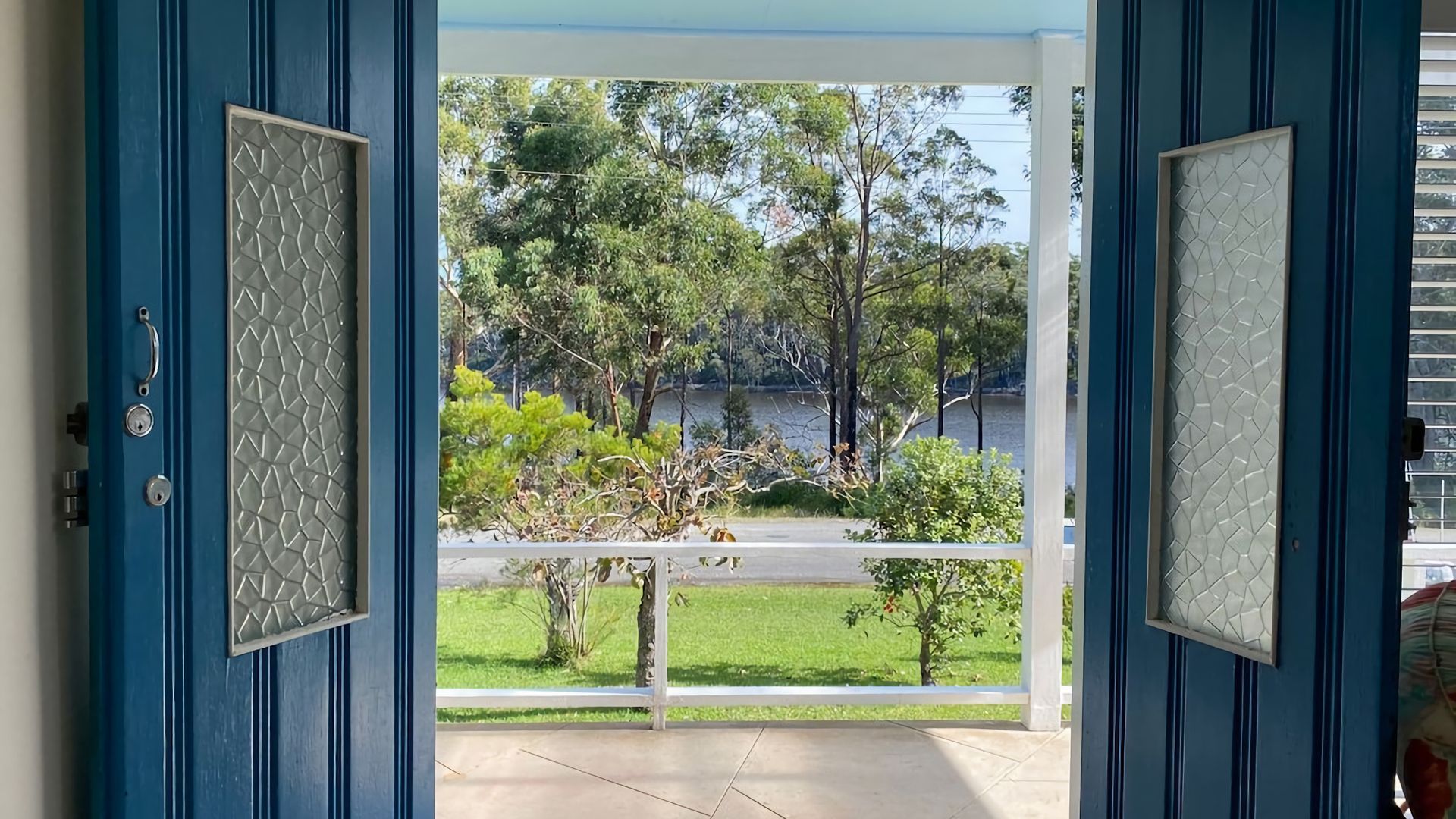 An open door with a view of a grassy area, trees, and a body of water.