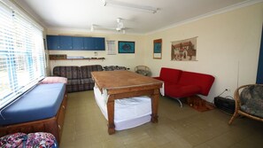 Ein Zimmer mit einem Bett, einem roten Sofa, einem Holztisch, einer blauen Bank und einem Fenster mit Jalousien.