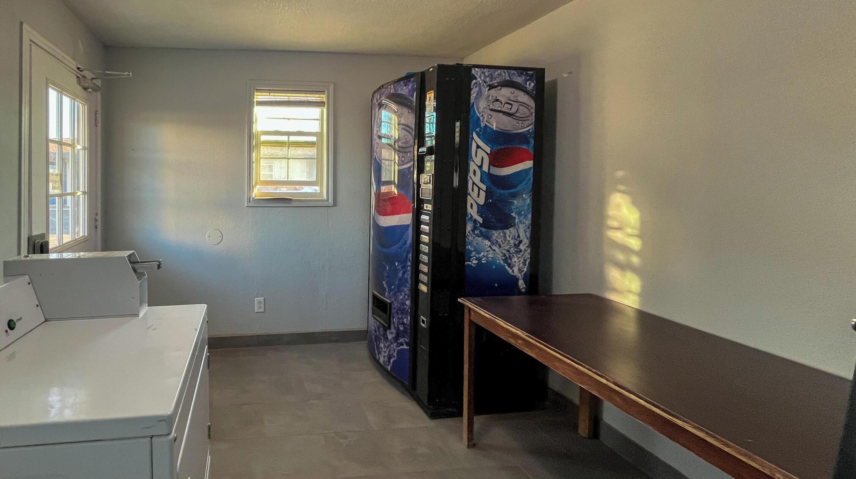 Ett rum med ett vitt skrivbord, ett litet fönster och försäljningsautomater med Pepsi-logotyper.
