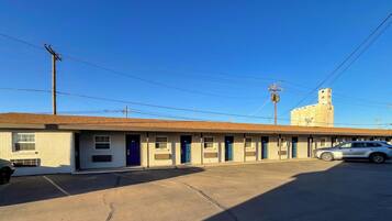 A motel with a row of rooms, a parking lot, and a building with a tower in the background.