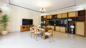 Una sala de estar moderna con comedor, televisor de pantalla plana y cocina con alacenas de madera y refrigerador negro.