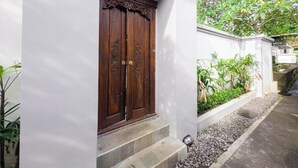 Una puerta de madera tradicional con elaboradas tallas, ubicada en una pared blanca con un escalón que la precede.