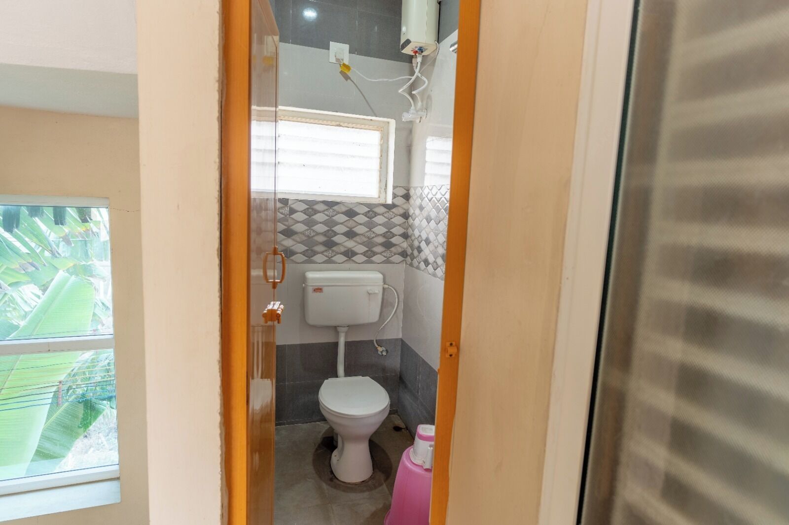 Un baño pequeño con inodoro, calentador de agua mural y ventana con persianas.