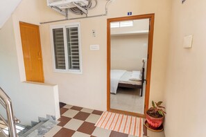 A hotel room with a bed, a window with blinds, a door, a staircase, and a potted plant. - KUKAL CASTLE (Tirupur)