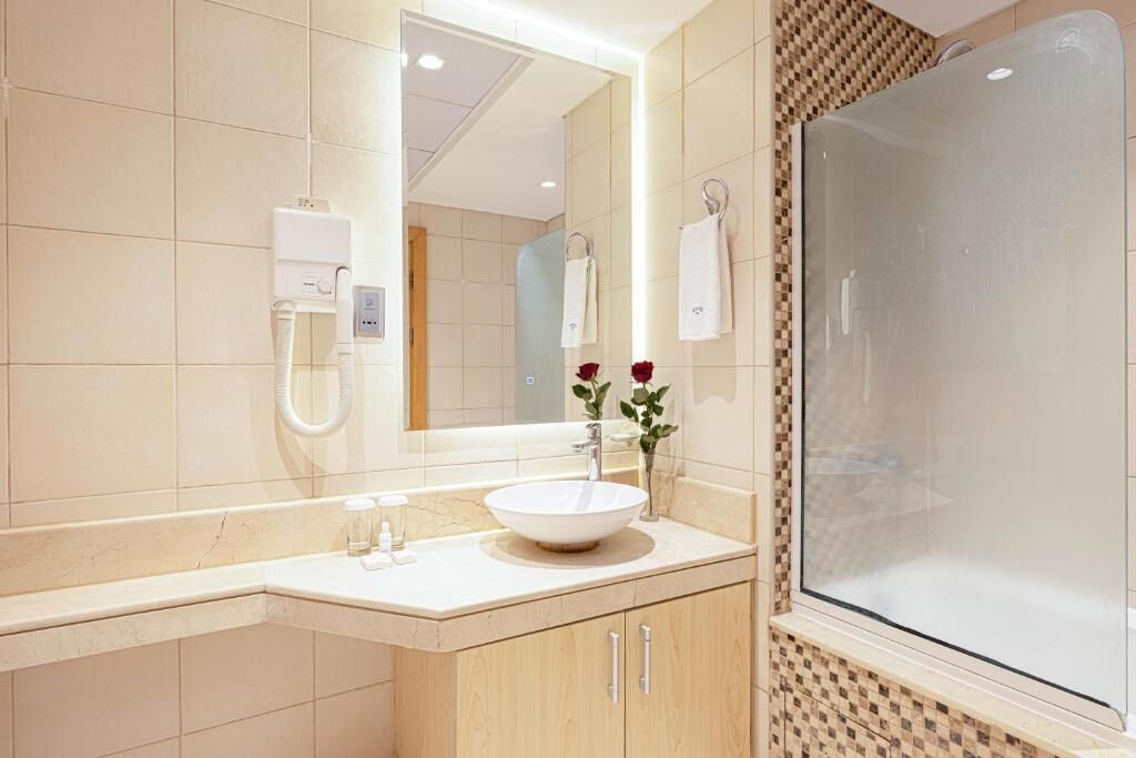 A modern bathroom with a large mirror, a white sink, a glass shower enclosure, and a towel rack.