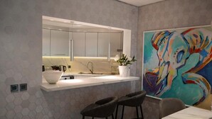 A modern kitchen with a white countertop, bar stools, and a colorful abstract painting on the wall. - Highend Shoreline Prestige Palm Jumeirah (Dubai)