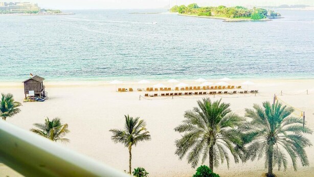 A beach with a row of sun loungers and a small wooden structure, likely a lifeguard hut, near the water. - Highend Shoreline Prestige Palm Jumeirah (Dubai)