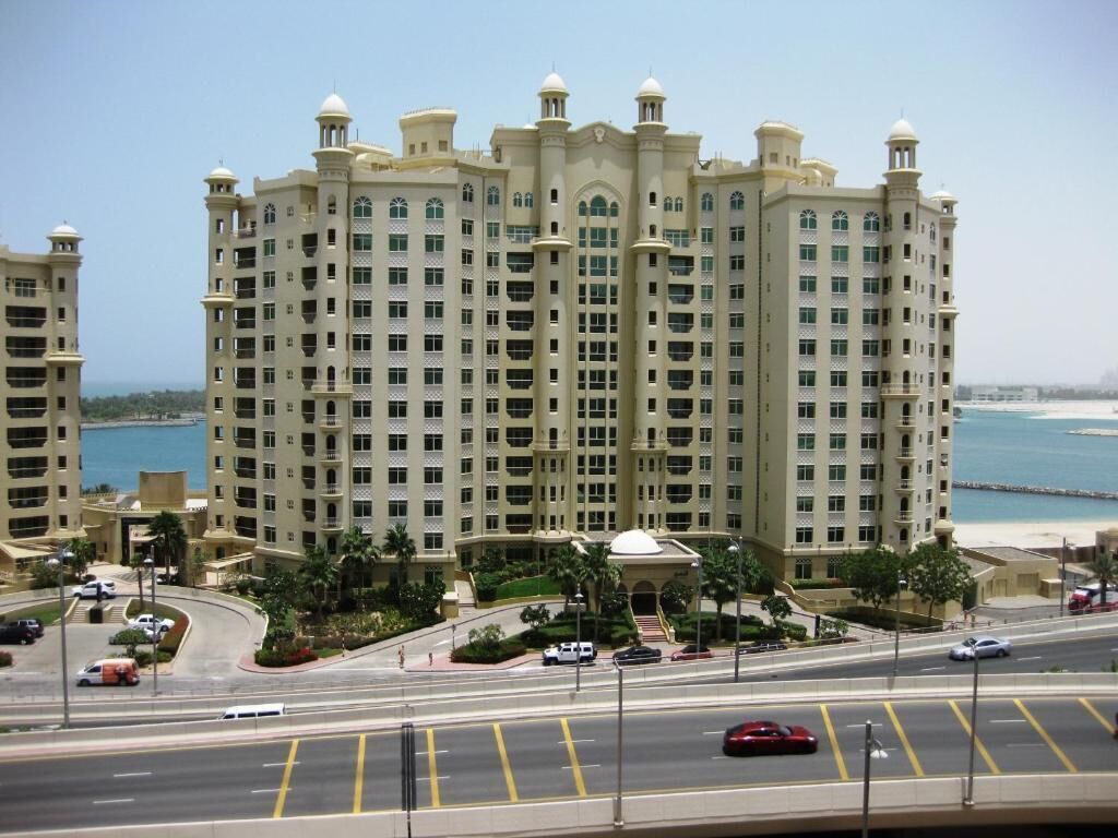 A multi-story hotel with a central courtyard, a beach view, and a parking area.