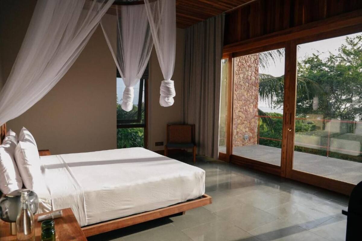 A bedroom with a bed, a nightstand, a chair, and a large sliding glass door leading to an outdoor area.