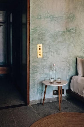 A room with a round table, a bottle, and glasses on a small table against a textured wall.