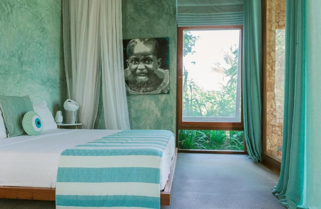 Un dormitorio con cama, ventana con cortinas, un cuadro en la pared y una mesita de noche con lámpara.